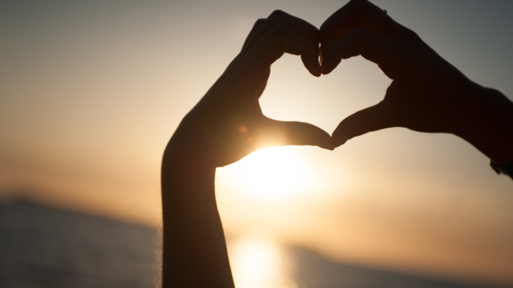 A silhouette of hands making a heart shape in front of a beautiful sunrise